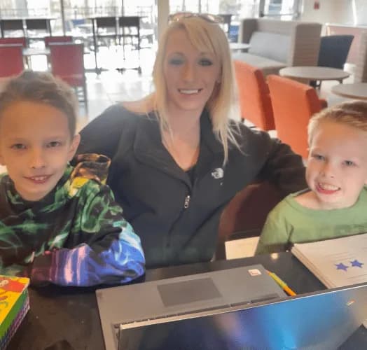 A teacher sitting with two students at a laptop