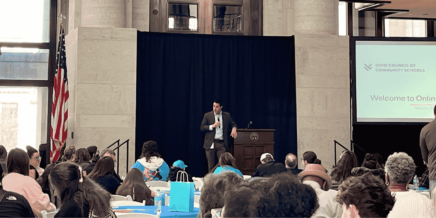 A speaker addresses an audience beside an Ohio Council of Community Schools presentation.